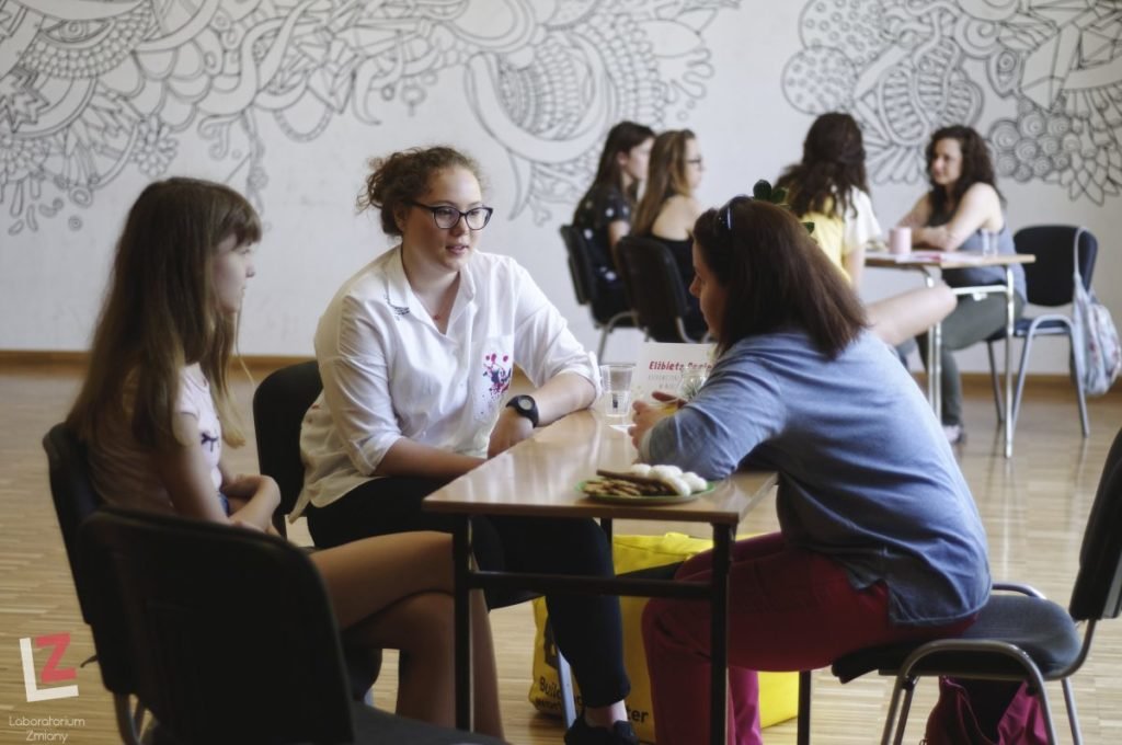 Dwie grupy osób siedzących przy stołach prowadzą rozmowę.