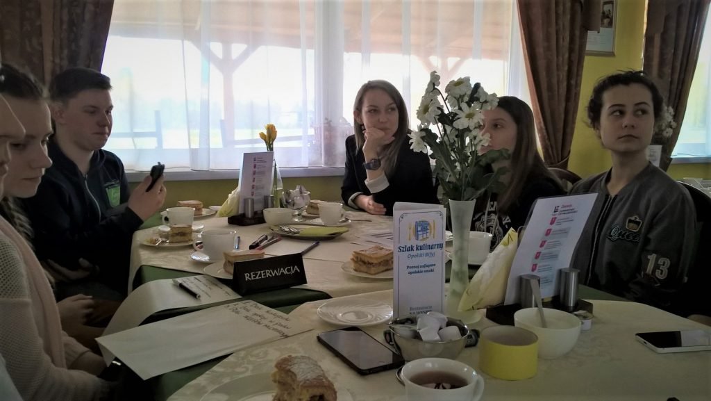 Cztery dziewczyny i chłopak siedzą w kawiarni przy zastawionym stole z napisem rezerwacja.