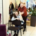 mężczyzna trzyma za ramiona siedzącą na krześle kobietę