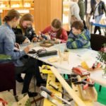 dziecko z pistoletem do silikonu w ręce skleja drewniane elementy