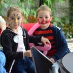 Dwójka dzieci, chłopiec i dziewczynka z pomalowanymi farbkami twarzami bawią się balonem.