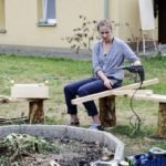 kobieta siedząca na ławce przy kręgu do ogniska z pomocą wiertarki zespala drewniane elementy.