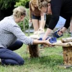 Dwie kobiety przecinają piłą drewniany element leżący na ławeczce.